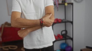 Spor salonunda spor salonunda spor aletleri, renkli ağırlıklar ve arka planda iplerle acı dolu dirseğini tutan bir adam..
