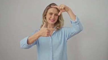 Sarışın kadının mutlu yüzü parmak çerçevesi yaparken yaratıcılığı ateşliyor! İzole edilmiş, genç bir fotoğrafçı tişört giyiyor, beyaz arkaplan resmine dikkat çekiyor..