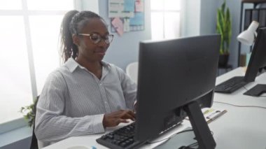 Ofiste çalışan güzel bir Afrikalı kadın bilgisayar kullanıyor ve gülümsüyor.