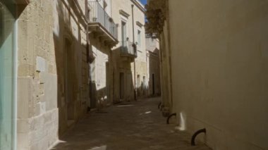 Tarih boyunca Lecce, Puglia, İtalya 'da balkonları ve karmaşık detayları olan eski taş binaların bulunduğu güneşli dar bir sokak..