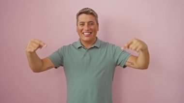 Kendine güveni tam, beyaz bir adam pembe arka planda gururla kendini işaret ediyor, mutlu ve kendinden emin.