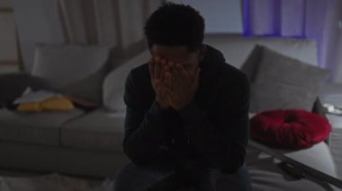 Düşünceli Afrikalı Amerikalı bir adam loş bir odada oturuyor, düşüncelere daldığını ve endişelendiğini söylüyor..