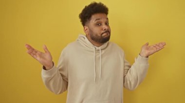 Şaşkın afro-amerikalı adam kapüşonlu kazak giyiyor. 'Bilmiyorum' jesti sarı bir duvar üzerinde. kuşkunun karışık ifadesi gösterildi.