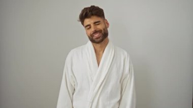 Bornoz giyen genç İspanyol bir adam göz kırpan mutlu bir yüzle kameraya bakıp izole edilmiş beyaz arka planda seksi bir ifadeyle neşeli görünüyor.