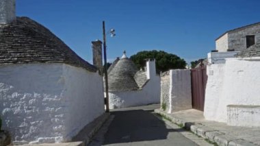Alberobello, Puglia, İtalya 'daki geleneksel trulli evlerin büyüleyici sokak manzarası. Açık mavi gökyüzünün altında beyazlatılmış duvarlar ve konik çatılar sergileniyor..