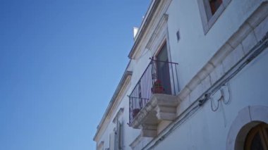 Locorotondo, puglia, İtalya, Avrupa 'da açık mavi gökyüzüne karşı beyaz bir taş bina üzerinde kırmızı çiçeklerle dolu bir balkon..