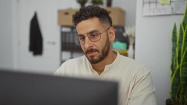 Ofis ortamında çalışan yakışıklı İspanyol bir adam ofis dekoru ve bitkilerle çevrili bilgisayar ekranına odaklanıyor..