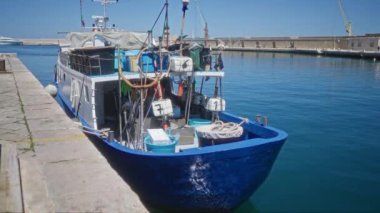 Mavi bir balıkçı teknesi Monopoli, İtalya 'da sakin bir limana yanaştı. Açık mavi gökyüzünün altında görünür ekipman ve iplerle otantik bir deniz manzarası yaratıyor..