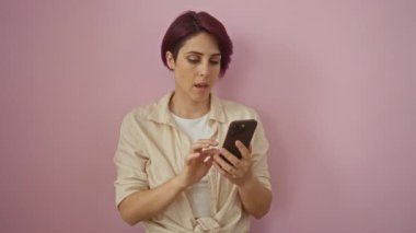 Kafkasyalı genç bir kadın kendine güvenen ve ciddi bir ifadeyle akıllı telefonu tutuyor. Savunma için dur işareti işareti kullanıyor. Pembe arka planda izole edilmiş.