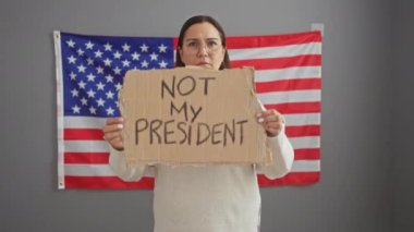 Yetişkin İspanyol kadın, Amerikan bayrağının önünde protesto işareti tutuyor..