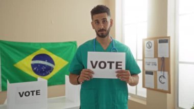 Arka planda Brezilya bayrağı olan bir üniversite odasında İspanyol asıllı genç bir adam 'oy' işareti tutuyor..