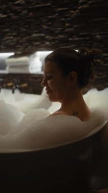 Huzurlu İspanyol bir kadın, loş ve rahat bir banyoda köpük banyosunun tadını çıkarıyor..