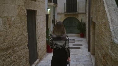 Genç bir kadın polignano 'nun büyüleyici sokaklarında yürüyor taş duvarlar ve büyüleyici bir Avrupa ortamında canlı saksılarla çevrili bir kısrak, puglia, İtalya.