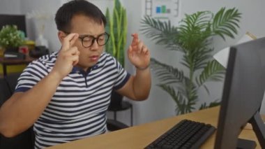 Ofisteki genç Asyalı bir adam bilgisayarın önünde heyecanla kutluyor ve dua ediyor..