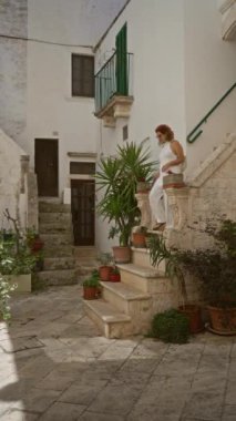 Genç İspanyol kadın locorotondo, puglia, İtalya 'da taş merdivenlerden iniyor. Etrafı saksı bitkileriyle ve tarihi beyaz binalarla çevrili..