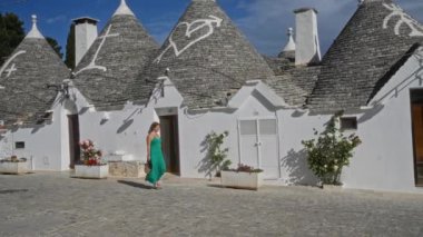 Genç bir İspanyol kadın güneşli bir günde eski Alberobello, Puglia, İtalya 'daki geleneksel Trulli evlerinin önünde yürüyor..