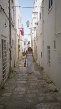 Beyaz elbiseli genç bir İspanyol kadın Puglia, İtalya 'nın eski caddelerinde yürüyor güneşli bir günde büyüleyici Avrupa mimarisini yakalıyor..
