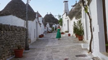Yeşil elbiseli genç bir İspanyol kadın geleneksel trulli evleri ve taş döşeli caddelerle çevrili İtalya 'nın eski Alberobello kasabasında yürüyor..