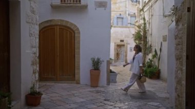 Genç İspanyol bir kadın polignano 'nun büyüleyici sokaklarında yürüyor. Puglia, İtalya' da beyaz binalar, saksılar ve huzurlu bir atmosfer ile çevrili bir kısrak..