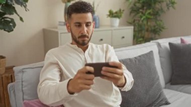 Genç bir İspanyol adam oturma odasında akıllı telefon ile oturuyor. Kapalı bir koltukta dinleniyor. Etrafı ev bitkileri ve yumuşak yastıklarla çevrili..