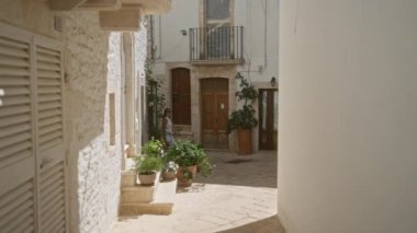 Genç bir İspanyol kadın, Puglia, İtalya 'da, etkileyici, eski, eski caddelerde yürüyor. Çevrelerinde geleneksel taş binalar ve canlı saksılar var..