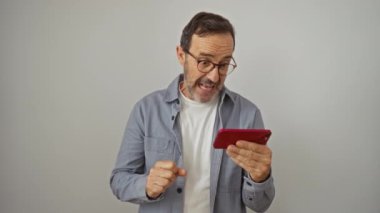 İspanyol adam başarıyı ve zaferi kollarını kaldırarak kutluyor, heyecanlı ve gururlu beyaz arka planda izole akıllı telefon kullanıyor.