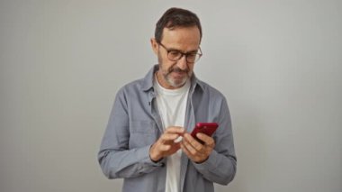 İspanyol orta yaşlı adam akıllı telefon tutuyor ve işaret veriyor. İzole edilmiş beyaz arka planda gülümsüyor, arkadaş canlısı, neşeli ve mükemmel bir sembol.