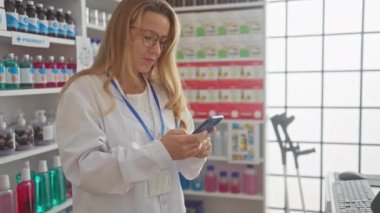 Modern eczanede akıllı telefon kullanan sarışın bir eczacı.