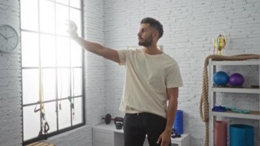 Genç, çekici İspanyol bir adam arka planda spor salonunda spor aletleriyle selfie çekiyor..