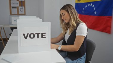 Genç, çekici, sarışın bir kadın, Venezuela 'daki demokratik süreci vurgulayan, Venezuela bayrağı ve oy işaretiyle işaretlenmiş, kapalı bir seçim okulunda oy veriyor..