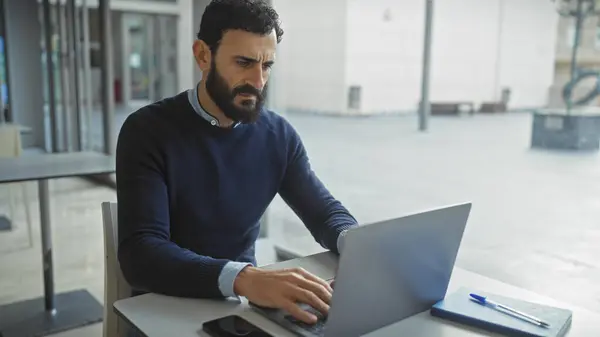 stock image Focused middle-aged man with beard working on laptop in modern office interior.