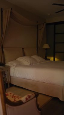 Lüks çarşafları olan şık bir yatak odası, çevre ışıkları ve alacakaranlıkta bir butik otelde çekilmiş modern bir fan..