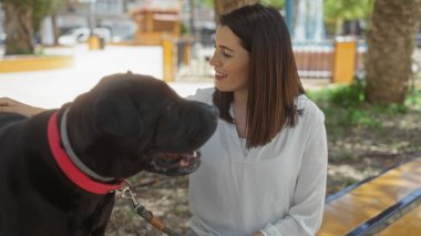 Parlak bir günde, şehir parkında labrador köpeğine gülümseyen genç İspanyol kadın..