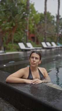 Genç bir kadın, tropik yeşilliklerle çevrili lüks bir bali otelindeki açık havuzda dinleniyor..