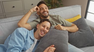 İki adam rahat bir oturma odasında kanepede birlikte rahatlıyor, sevgi ve mutluluk sergiliyorlar, gay, Igbt, çift ve aile temalarını vurguluyorlar.
