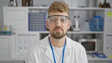 Mavi gözlü, sakallı ve güvenlik gözlüklü beyaz önlüklü, kapalı bir laboratuvar ortamında beyaz önlüklü beyaz bir beyaz adamın portresi..