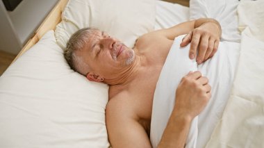 Sıkıntılı orta yaşlı bir adam yatağında yatıyor. Sanki acı, rahatsızlık ya da kötü bir rüya görüyormuş gibi yüzünü buruşturuyor..