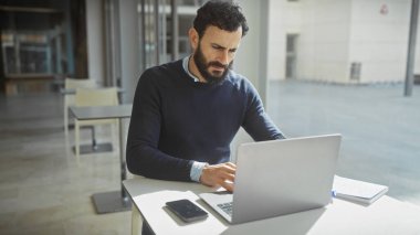 Modern ofiste dizüstü bilgisayarla çalışan odaklanmış sakallı adam profesyonellik ve konsantrasyon gösteriyor..