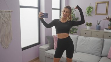 Kafkasyalı genç bir kadın hoş, mor bir oturma odasında esnek bir selfie çekiyor.