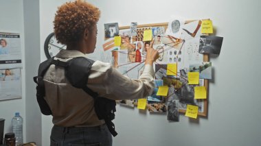 African american woman detective analyzes evidence board in police station office. clipart