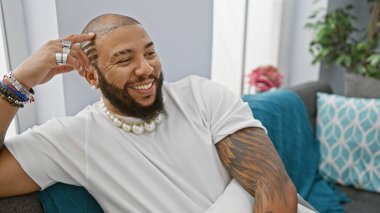 Gülümseyen Afrikalı Amerikalı adam şık bir oturma odasında takı takarak uzanıyor.