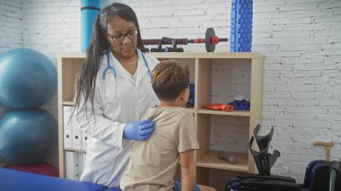 Bir kadın doktor, rehabilitasyon kliniğinde tedavi malzemeleriyle dolu olan bir çocuğu muayene ediyor..