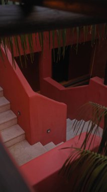 Mimari görüntü, sakin, kentsel bir ortamda tropikal bitkilerle dolu açık kırmızı bir merdiven gösteriyor..