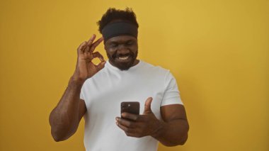 Sakallı, yakışıklı, Afro-Amerikan bir adam akıllı telefon kullanıyor ve sarı bir arka plana işaret ediyor..