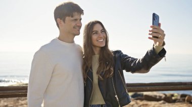 Gülümseyen bir çift deniz kenarında selfie çeker, ilişkilerini gösterirler ve güneşli hava manzarasının tadını çıkarırlar..