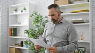 Sakallı, olgun bir İspanyol modern ofis ortamında bir belge okuyor..