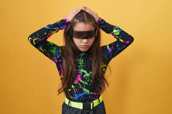 stock image Adorable hispanic girl agonizing with stress headache, suffering migraine pain. sad child with vr glasses, hands on head, isolated on yellow background.