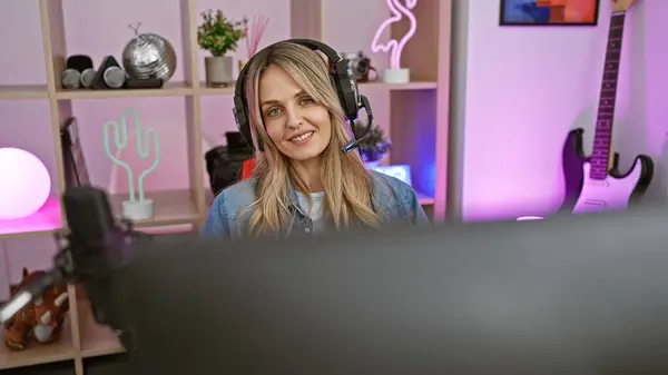 stock image Attractive young woman with headphones in gaming room lit with neon lights smiling at the camera