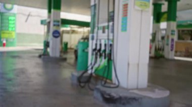Arka planda yeşil ve beyaz yakıt pompaları ve tabelaları olan bir açık hava benzin istasyonu görüntüsü bulanık, bokeh etkisi yaratıyor.