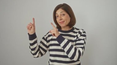 Çizgili bir kazak giymiş neşeli, orta yaşlı İspanyol bir kadın şakacı bir şekilde kenarı işaret ediyor. Kendine güveni tam, izole edilmiş beyaz bir arka planda kameraya gülümsüyor..